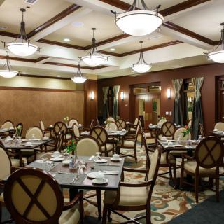 An elegant dining room setup with multiple tables and chairs, featuring stylish chandeliers and a classic interior design.