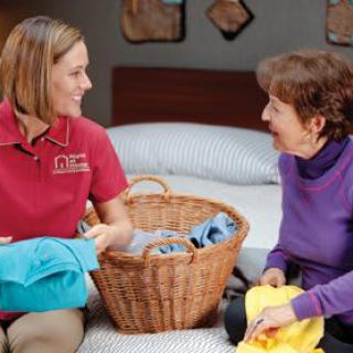 A caregiver assists an elderly woman with laundry, engaging in a friendly conversation.