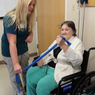 A healthcare professional assists an elderly patient in a wheelchair during a physical therapy session.