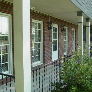 A porch with brick walls and multiple windows, featuring railings and greenery.