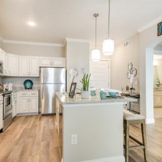 A modern kitchen with stainless steel appliances and white cabinetry, featuring pendant lighting and wood flooring.