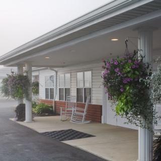 A building entrance with a covered porch, adorned with hanging plants and rocking chairs.