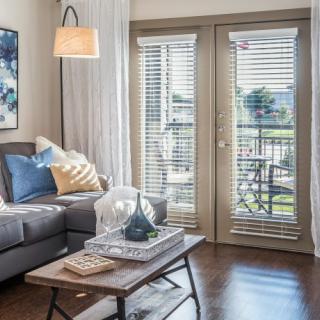 A cozy living room with a modern gray sofa, decorative cushions, and a stylish coffee table in front of French doors with blinds.