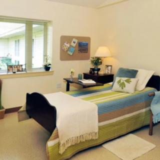 A cozy bedroom with a single bed, a window, and warm lighting from a bedside lamp.