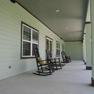 A covered porch with multiple rocking chairs and windows along the wall.