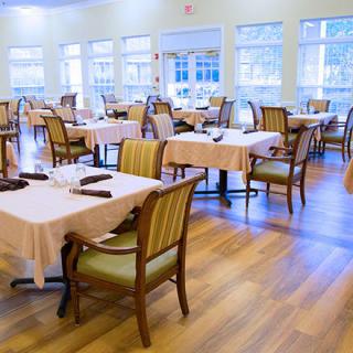 An empty dining room with neatly arranged tables and chairs, illuminated by natural light from large windows.