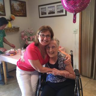 Two people smiling and hugging during a celebration indoors, with a balloon in the background.
