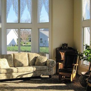 A cozy living room with a sofa and chair, bathed in sunlight streaming through large windows.