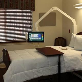 A hospital room featuring a bed with an adjustable table and a monitor attached.