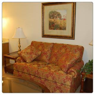 A cozy living room with a patterned sofa, artwork on the wall, and a lamp on a side table.