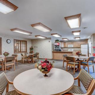 A communal dining area with tables, chairs, and a kitchen in the background.
