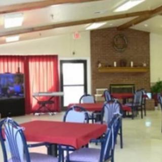 A community dining area with tables covered in red tablecloths and a brick fireplace.