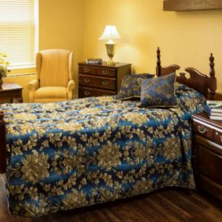 A cozy bedroom featuring a single bed with a floral quilt, a wooden nightstand, and a yellow armchair.