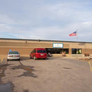 A school building with cars parked in front and an American flag flying overhead.