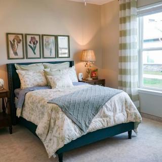 A cozy bedroom with a neatly made bed, artwork on the wall, and a large window.