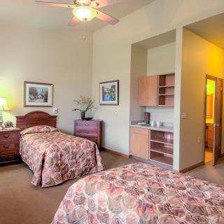 A cozy bedroom with two single beds, warm lighting, and a small kitchenette.