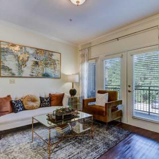 A stylish living room featuring a modern sofa, glass coffee table, and artwork on the wall, with large windows leading to a balcony.