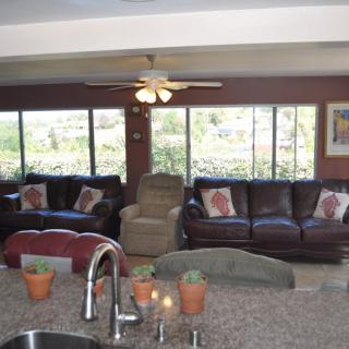 A cozy living room with large windows, sofas, and a ceiling fan.