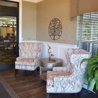 A cozy lobby with two patterned chairs, a small round table, decorative wall art, and a potted plant.