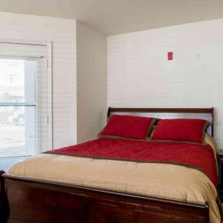 A neatly made bed with red and beige bedding in a bright bedroom.