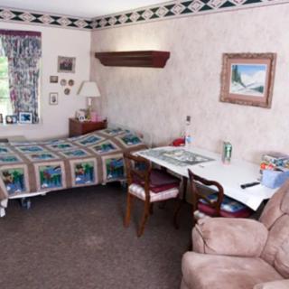 A cozy bedroom with a quilt-covered bed, a desk with chairs, and wall decor.