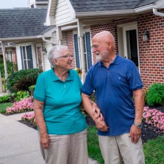 An elderly couple enjoys a moment together in their picturesque neighborhood, holding hands and sharing smiles.