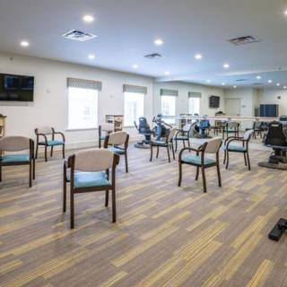 A spacious exercise room with chairs and fitness equipment arranged on a wooden floor.