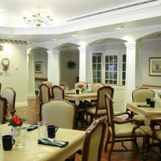 A cozy dining area featuring elegantly arranged tables and chairs, illuminated by a chandelier.