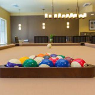 A set of billiard balls neatly arranged on a pool table in a well-lit recreation room.