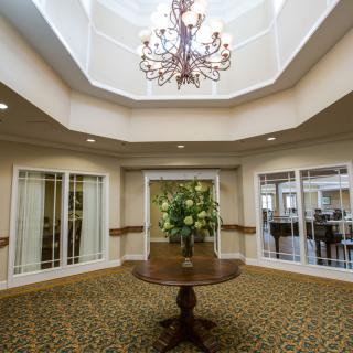 A well-lit lobby with a chandelier, a central table with floral decor, and carpeted flooring.