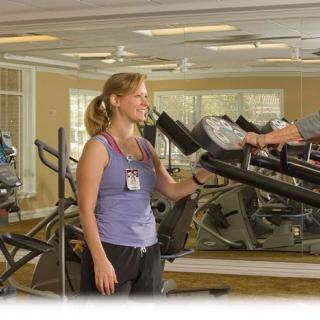A trainer assists a person on a treadmill in a gym setting.
