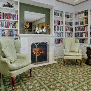 A cozy library with bookshelves, armchairs, and a fireplace.