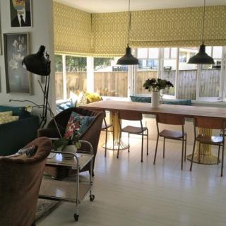 Modern living room with a long table and chairs, featuring large windows and stylish lighting.