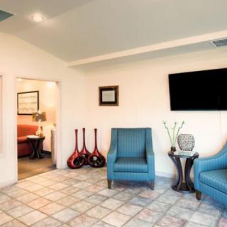 A modern waiting room with blue chairs, a wall-mounted television, and guitars on a stand.