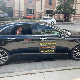 A driver waving from a black car with signage for a transportation service.