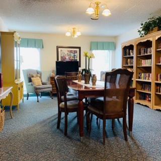 A cozy living space with bookshelves, a central table surrounded by chairs, and comfortable seating areas near the window.