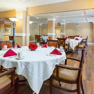A well-set dining area with elegantly arranged tables and chairs, featuring red napkins and wooden flooring.