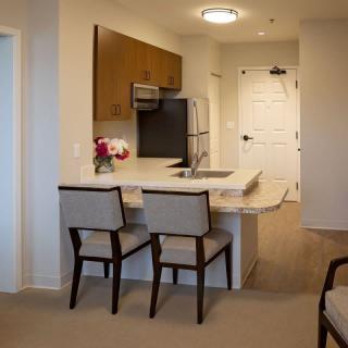 A modern kitchen area in an apartment with a countertop and chairs.