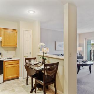 A cozy kitchen and dining area featuring wooden cabinets, a small dining table with chairs, and an open layout leading to the living room.