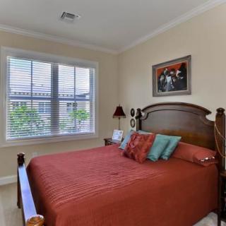 A cozy bedroom with a bed adorned with colorful pillows, a window providing natural light, and decorative artwork on the wall.