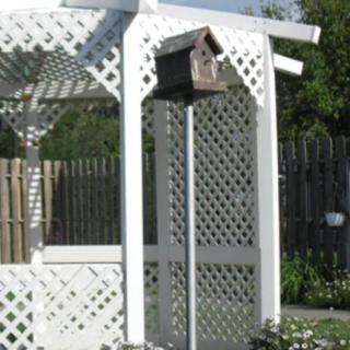 A white lattice arbor with a birdhouse in a garden setting.