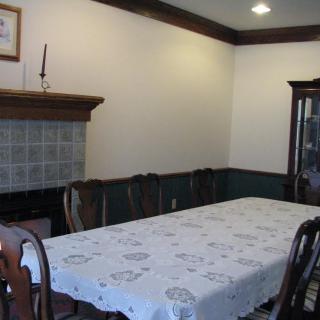 A dining room with a long table covered in a white tablecloth, surrounded by chairs and featuring a fireplace with a mantel.