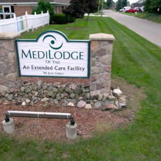 A sign for MediLodge, an extended care facility, surrounded by landscaped grass and a stone base.