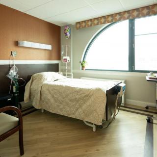 A hospital room with a bed, large window, and medical equipment.