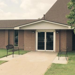 A brick building entrance with chairs on a sidewalk leading up to glass doors.