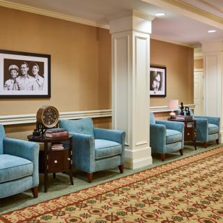 A cozy lobby area featuring blue armchairs, decorative tables, and framed artwork on the walls.