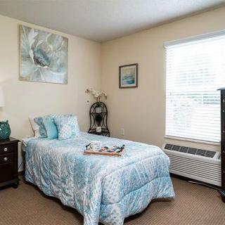 A cozy bedroom with a single bed decorated in blue tones, featuring a window and wall art.