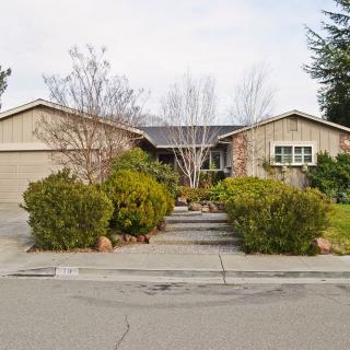 A suburban house with a landscaped front yard featuring trees and bushes.