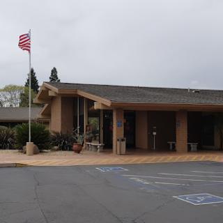 A building with an American flag and handicap parking spaces in front, under an overcast sky.