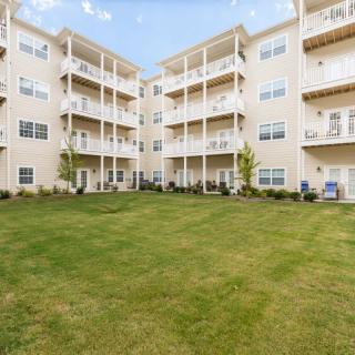 A modern apartment complex with multiple stories and balconies, surrounded by a well-maintained lawn.